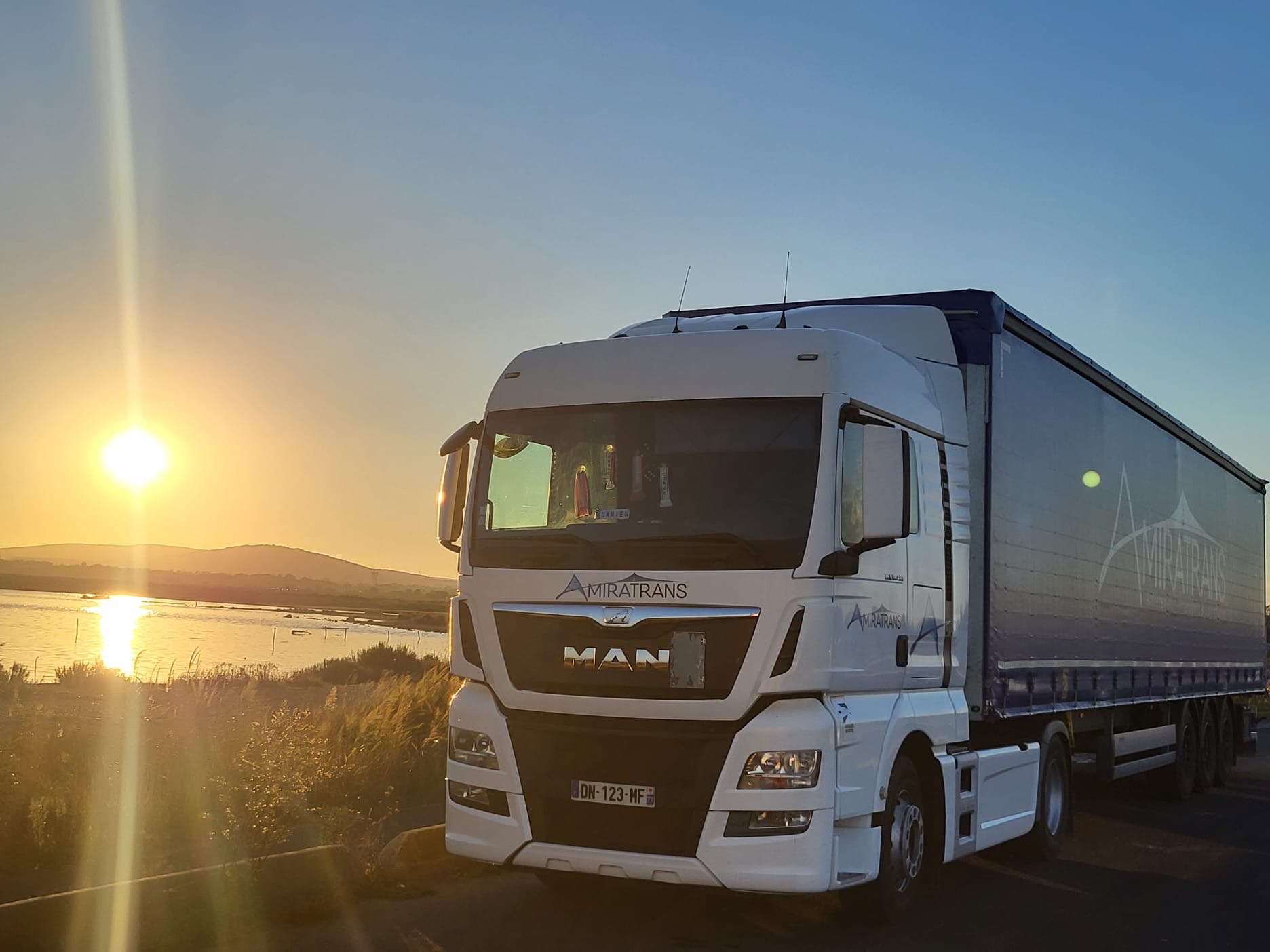 Semi-remorque Amiratrans tautliner roulant sur l'autoroute A9 en direction de l'Espagne, au lever du soleil, ciel orangé sur fond de garrigue méditerranéenne